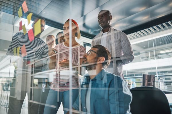 Image of people working as a group planning out and collborating on a clear notice board